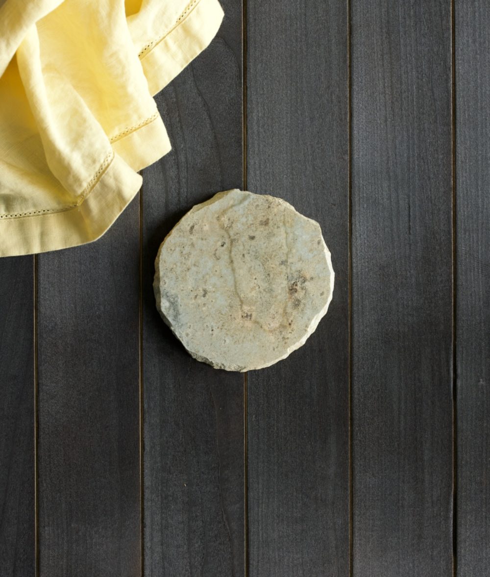 metamorphic stone coaster with yellow, white and green colors with yellow white napkin on top of a wooden background