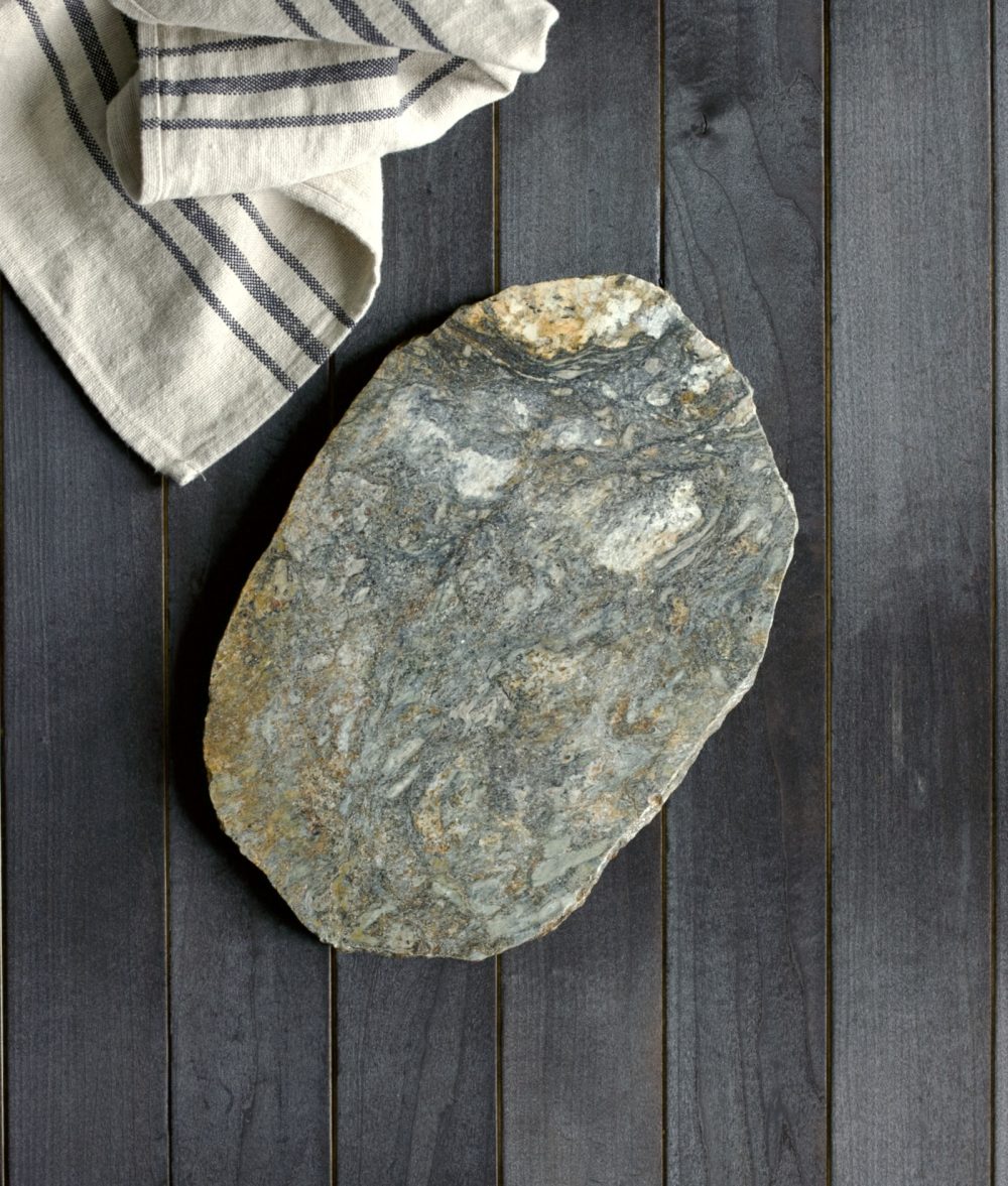 metamorphic stone coaster with green, white and yellow colors with white napkin on top of a wooden background
