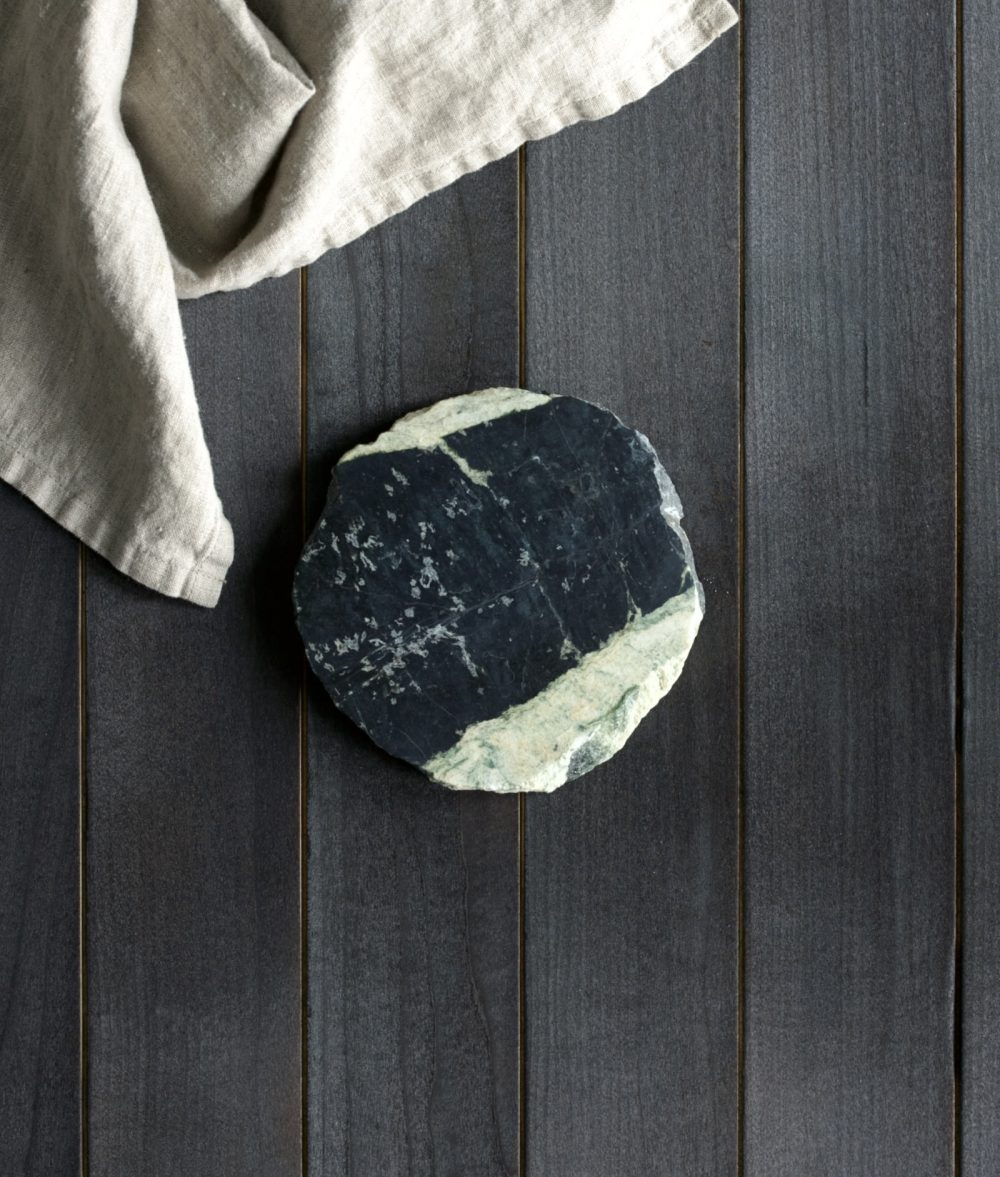 metamorphic stone coaster with yellow, white and green colors with white napkin on top of a wooden background