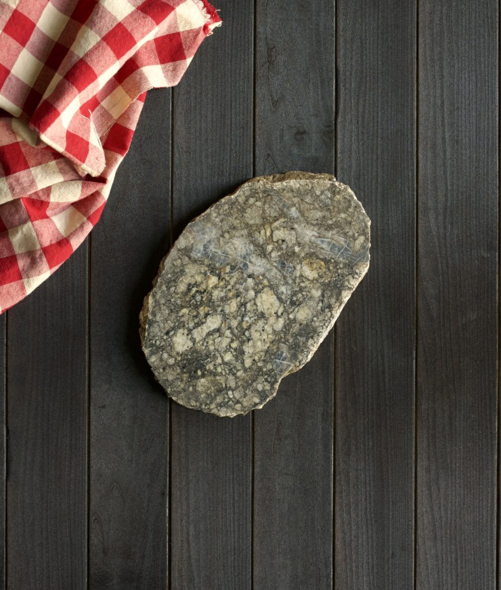 metamorphic stone trivet with gray and yellow colors on top of a wooden background with red and white napkin
