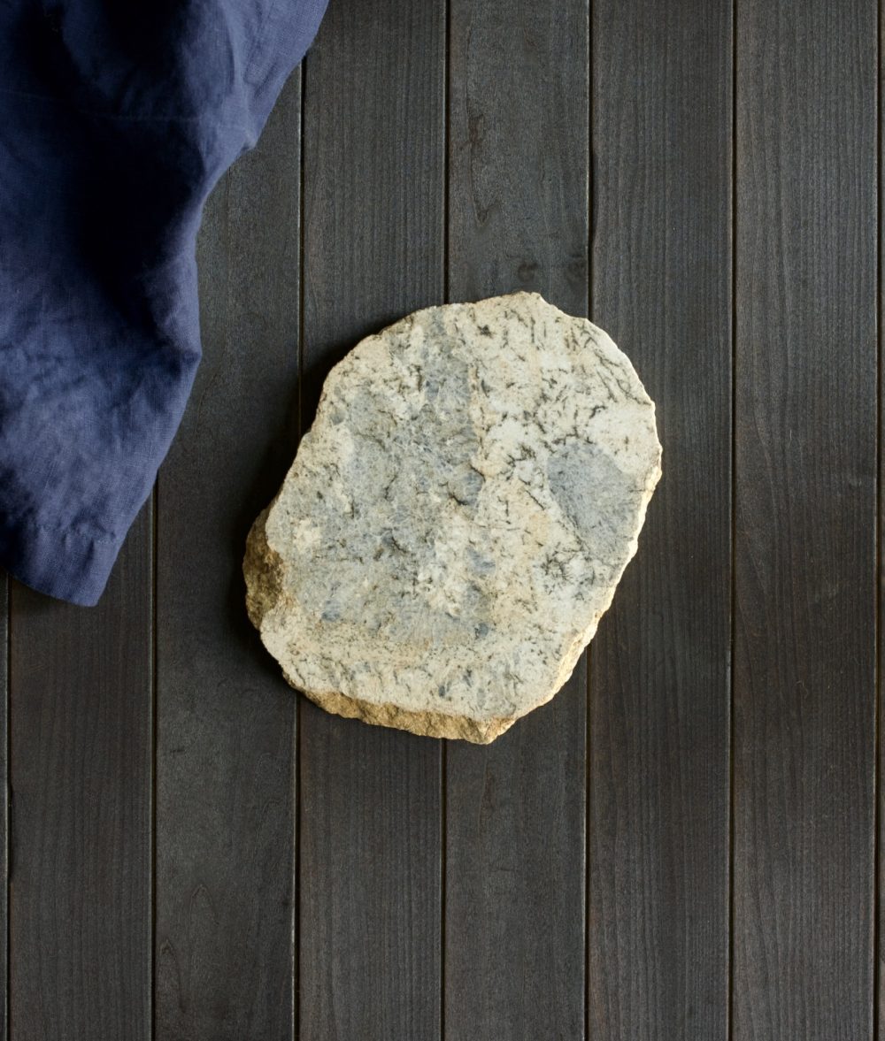 metamorphic stone trivet with gray and yellow colors on top of a wooden background with blue napkin