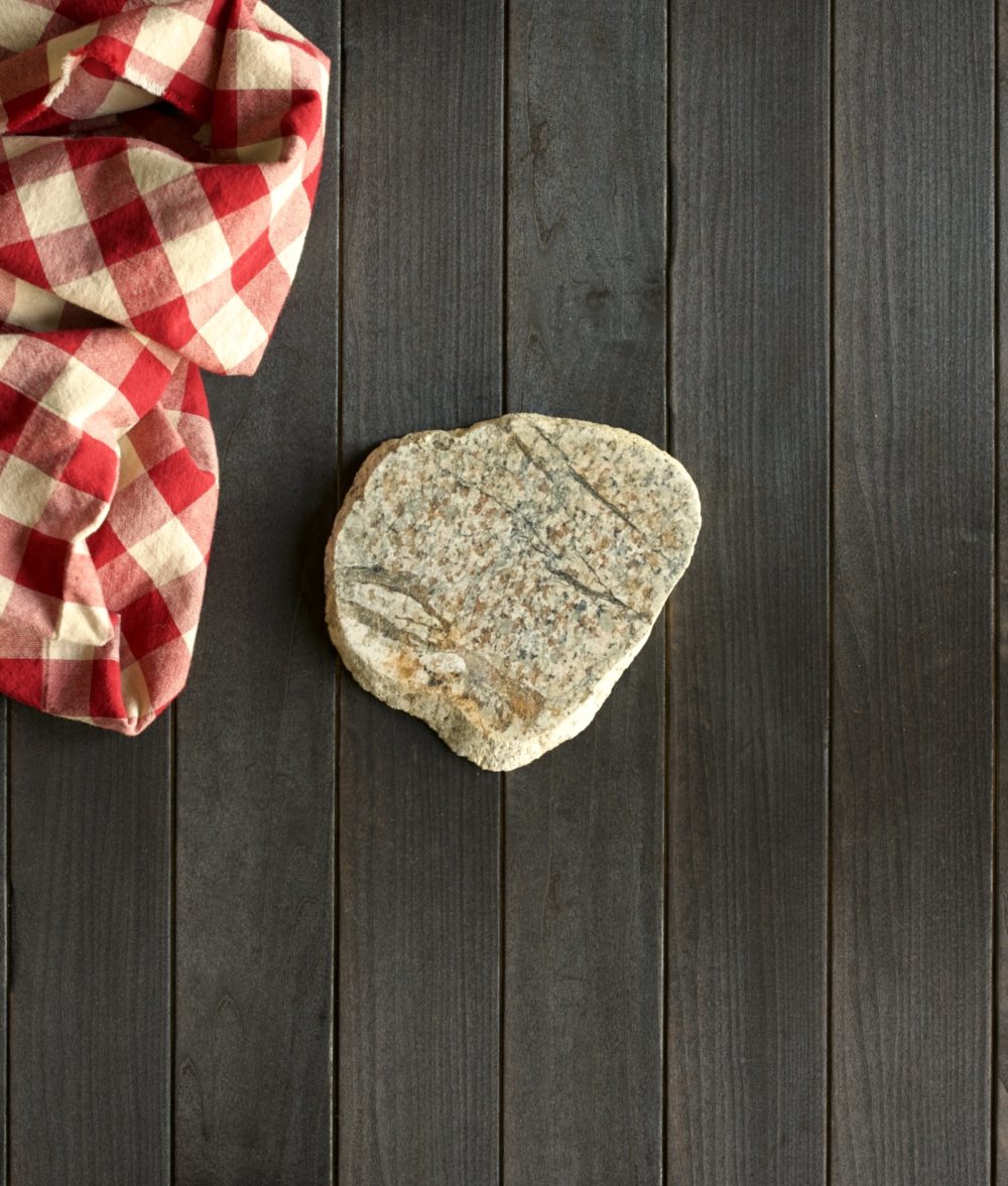 metamorphic stone trivet with gray and yellow colors on top of a wooden background with red and white napkin