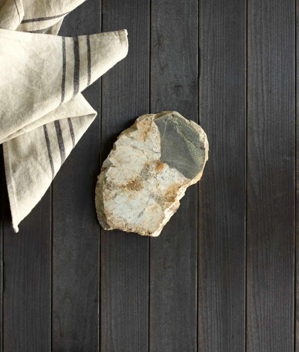 metamorphic stone trivet with gray and yellow colors on top of a wooden background with white napkin