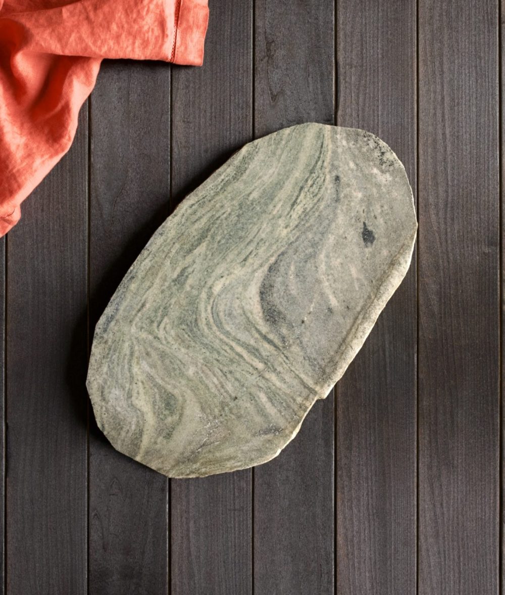 metamorphic stone charcuterie board with gray, green and white colors with orange napkin on top of a wooden background